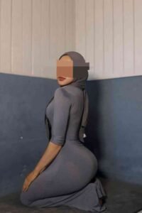 Elegant Malay Escort in KL, reflected in a mirror, wearing a hijab and a black dress. Girl Service.