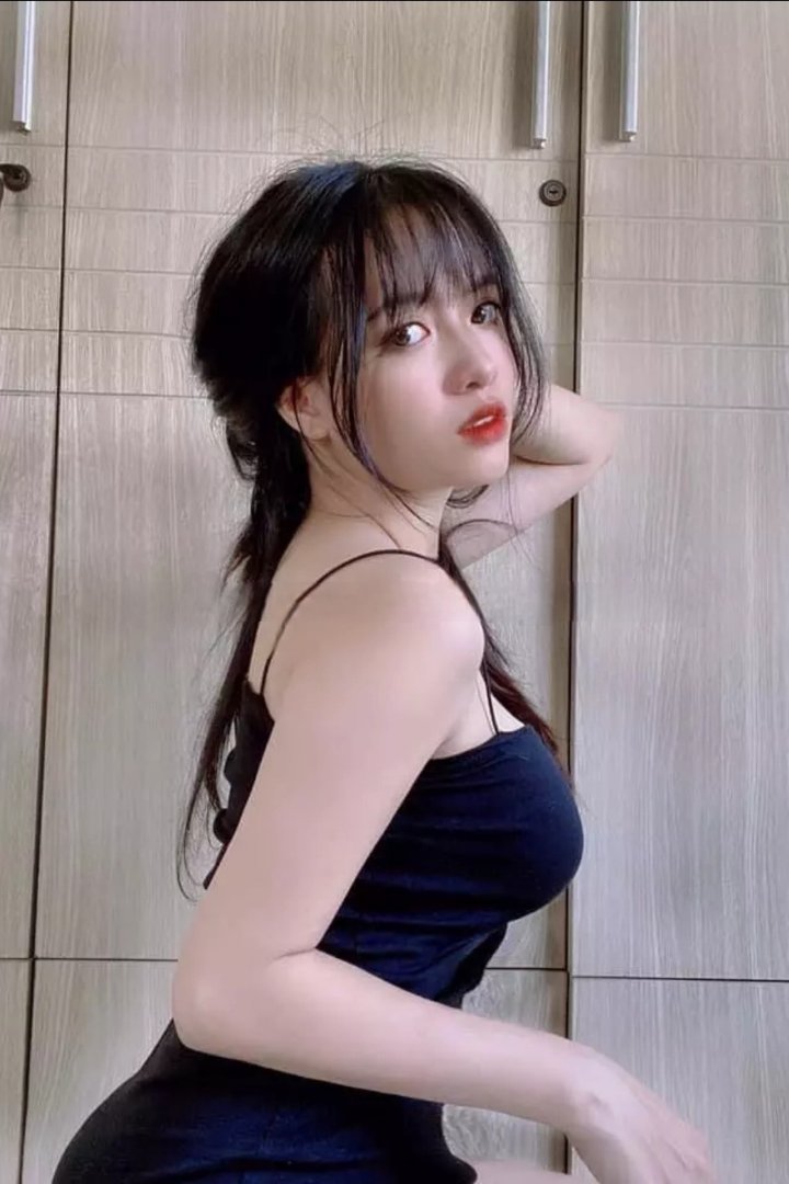 Young woman in black dress poses against a wooden cabinet. Malay Escort, KL Escort, Malaysia Escort