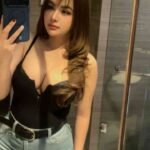 Woman in black top and jeans taking a mirror selfie.